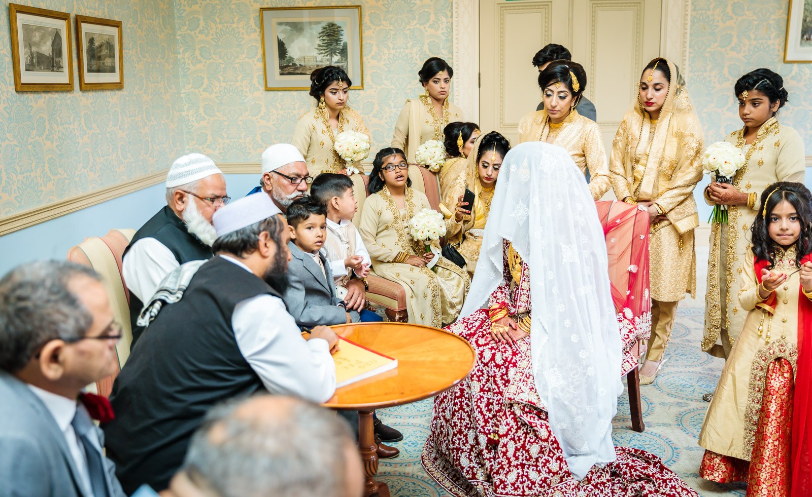 The bride sits veiled in red amid family as elders lead the nikah