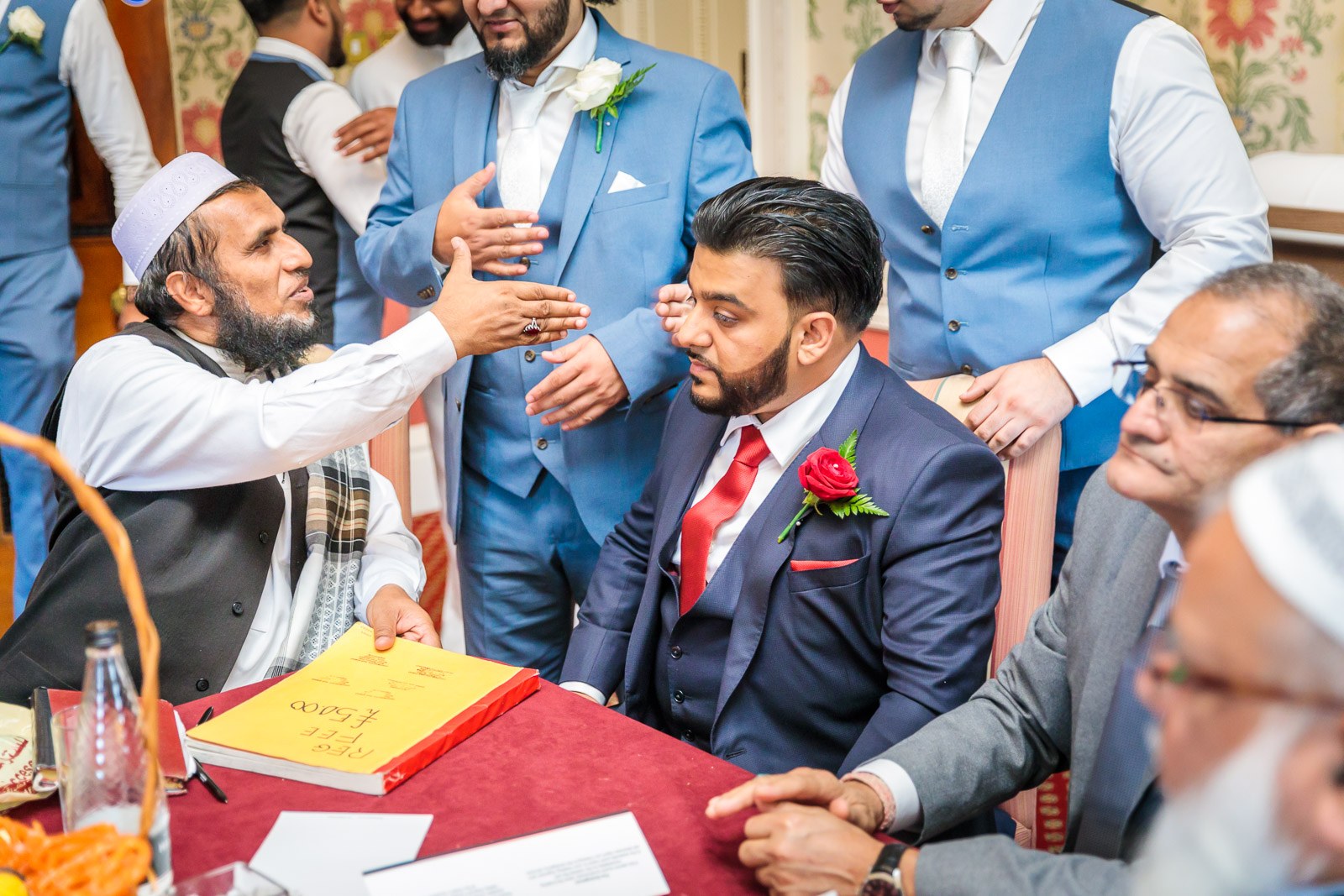 An elder reaches across to bless the groom at the signing table