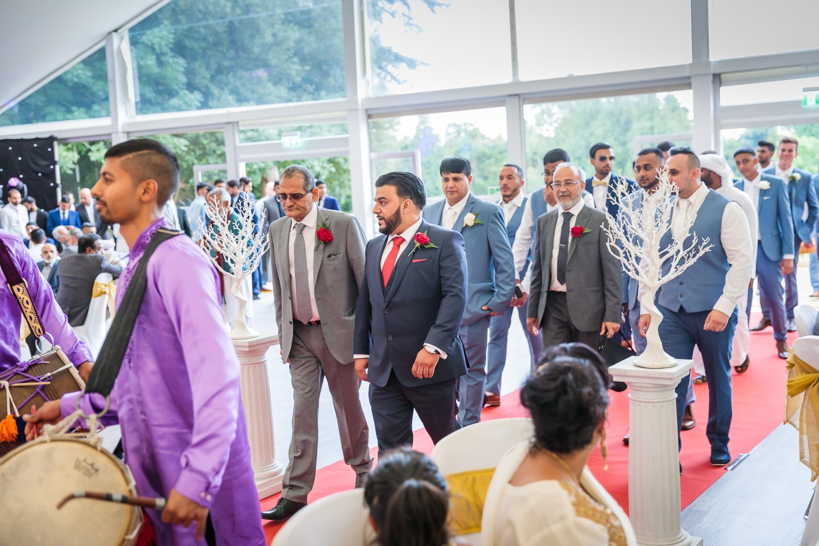 A dhol drummer leads the procession up the red carpet into the marquee