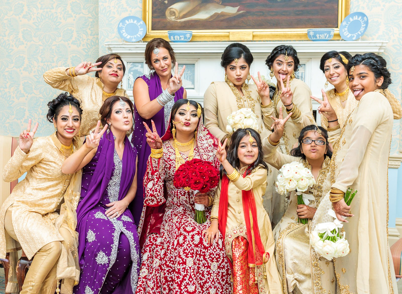 Women and girls in gold and purple pose with the bride, flashing peace signs