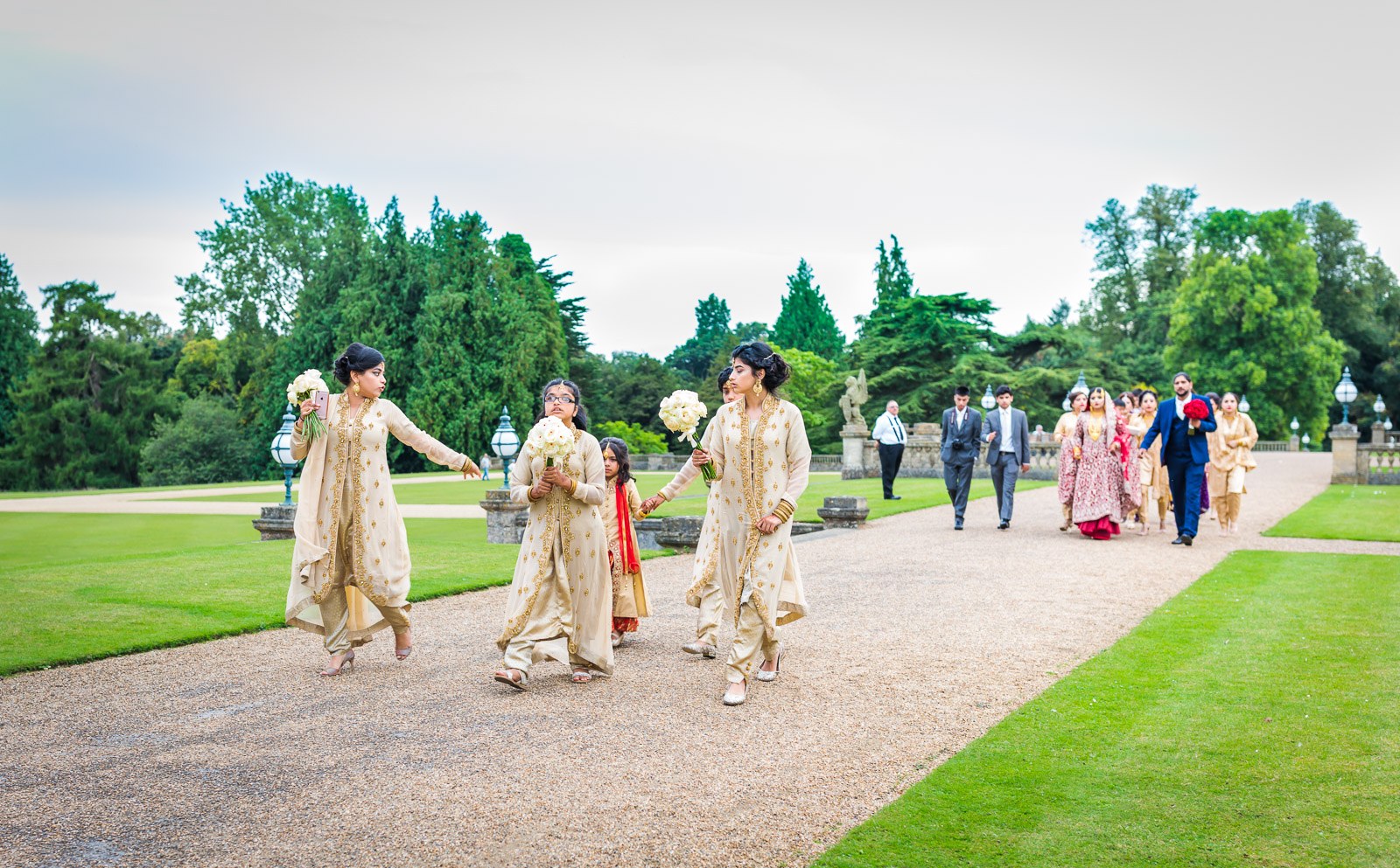 The couple cross the gardens of Heythrop Park with their wedding party