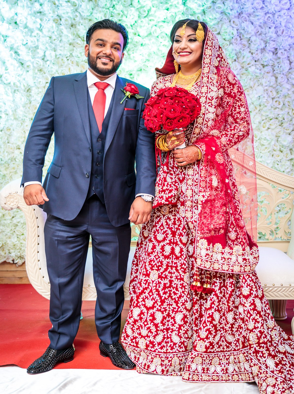 The couple stand together on the stage before the white flower wall