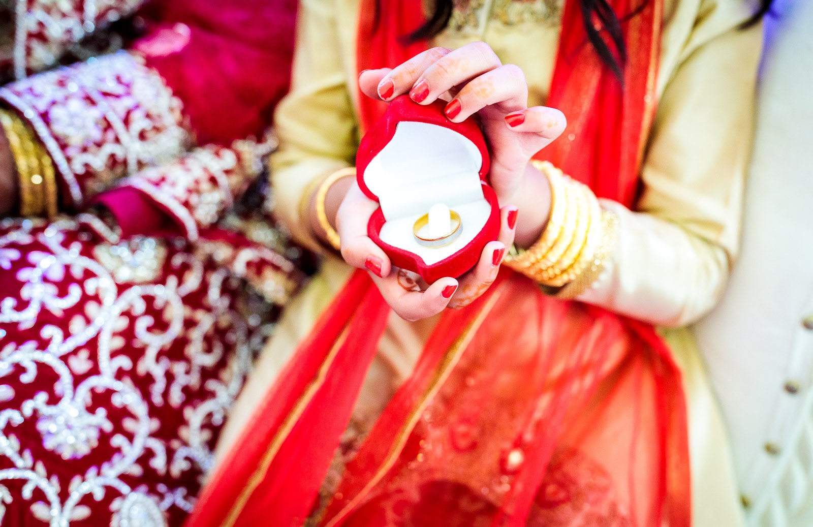 Close-up of hennaed hands with gold bangles holding an open ring box