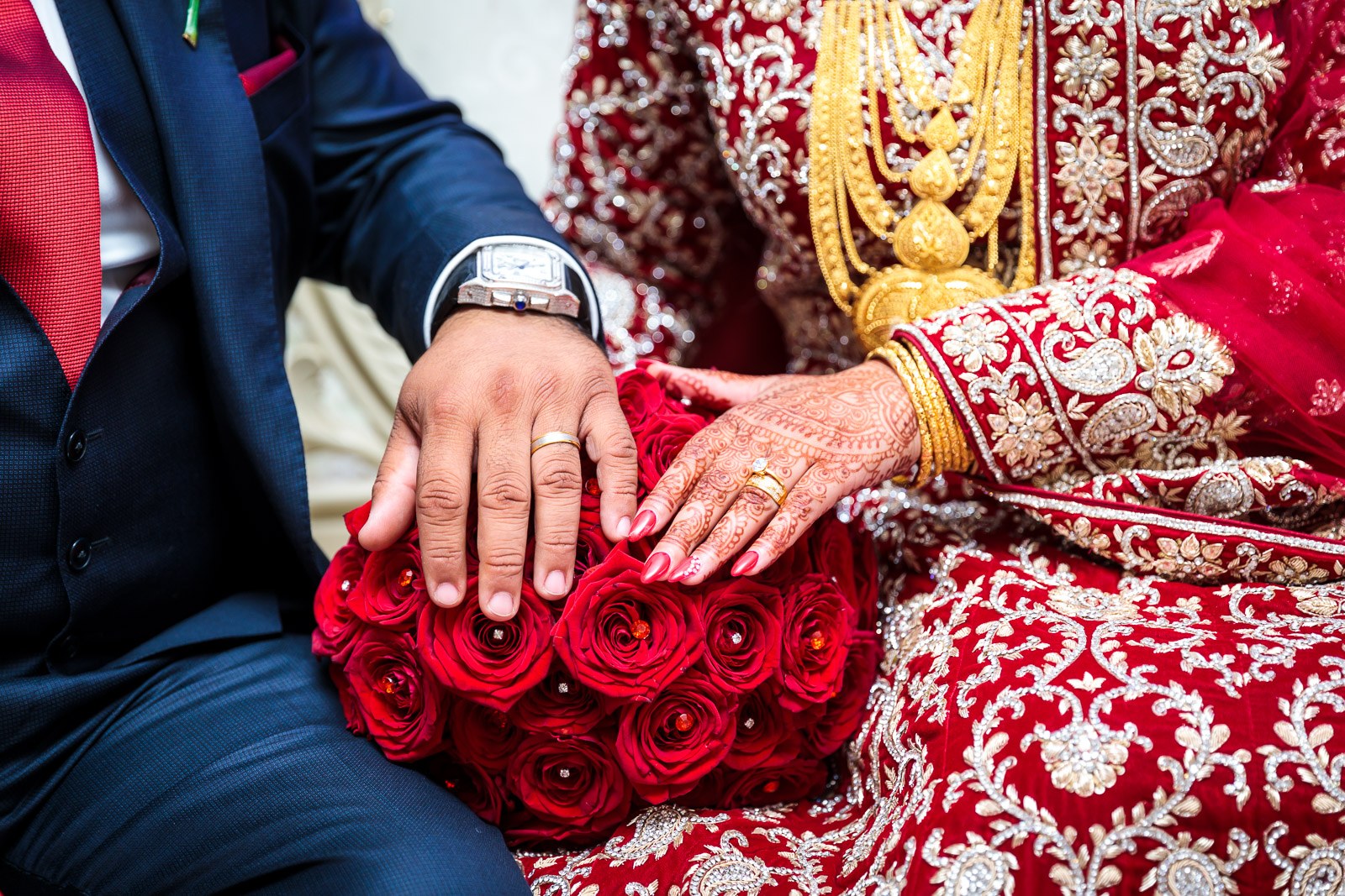 Close-up of the ring on the bride's hennaed hand over her red bouquet