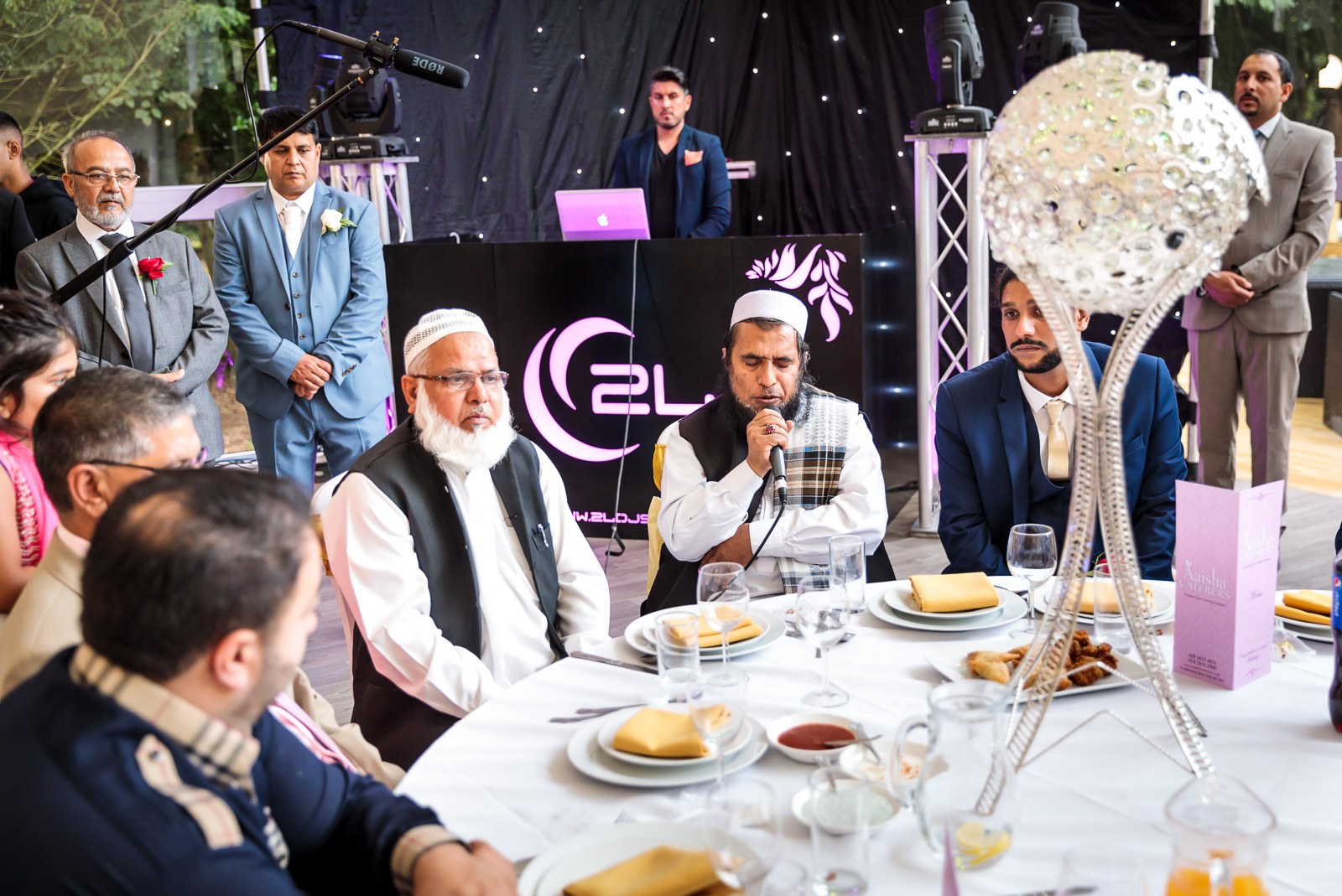 An elder speaks into a microphone at the top table in the marquee