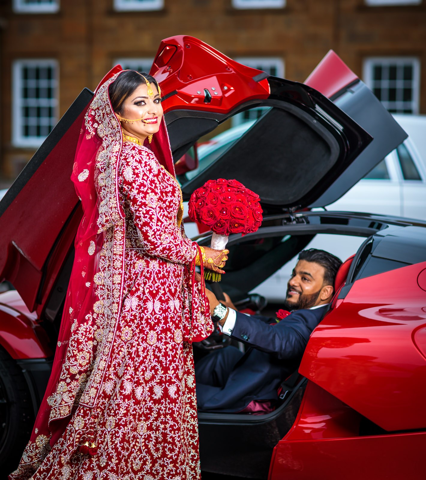The bride smiles beside the open Ferrari door as the groom sits at the wheel