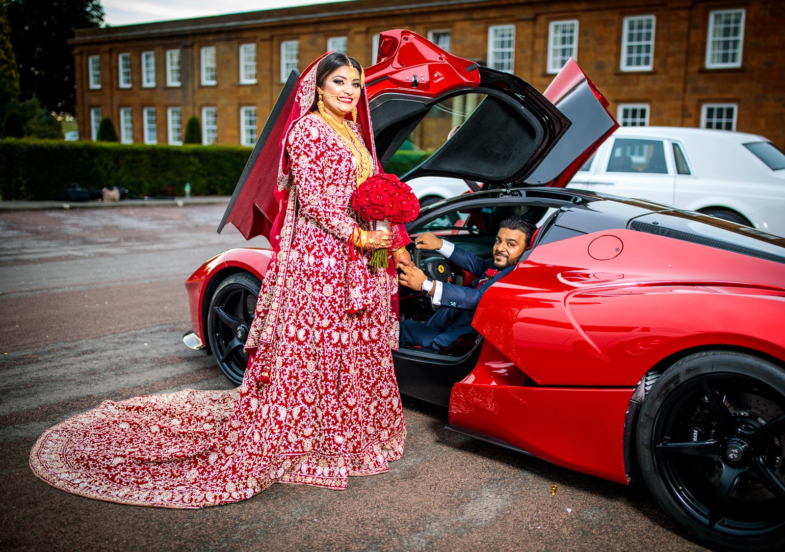 The bride stands by the gullwing door of the red Ferrari outside Heythrop Park