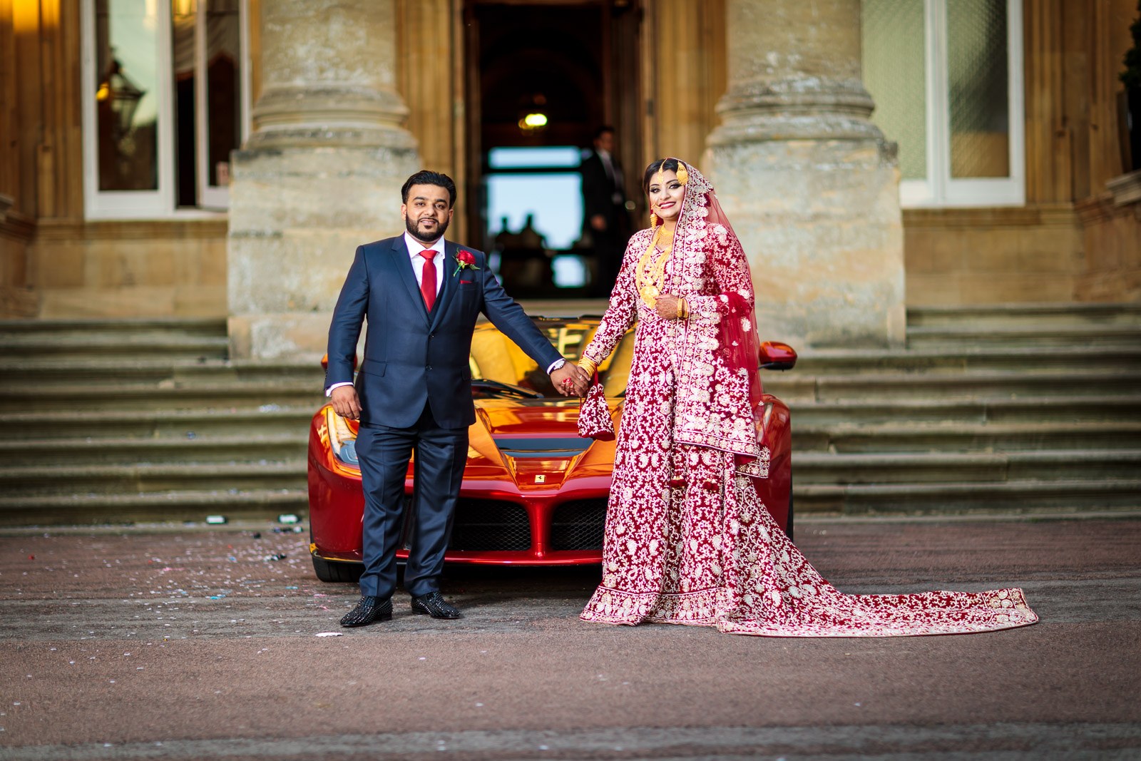 The couple and the red Ferrari before the golden-lit facade of Heythrop Park