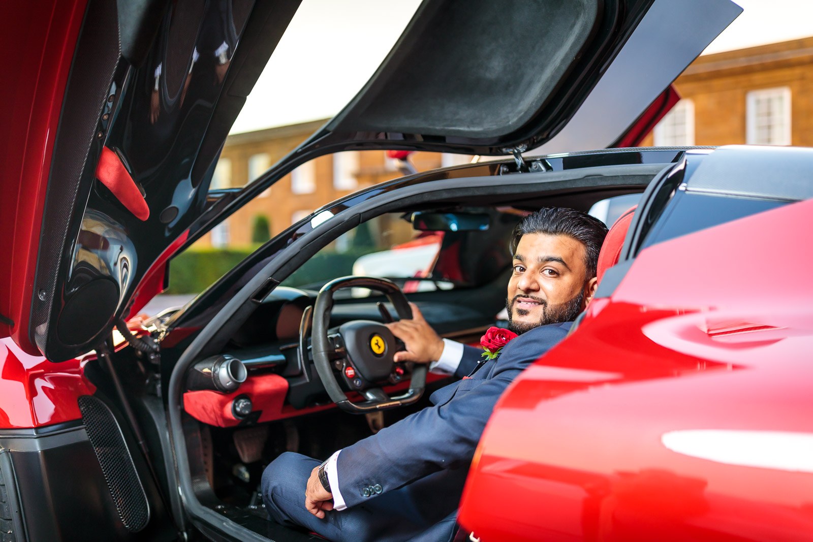The groom sits at the wheel of the red Ferrari, gullwing door raised