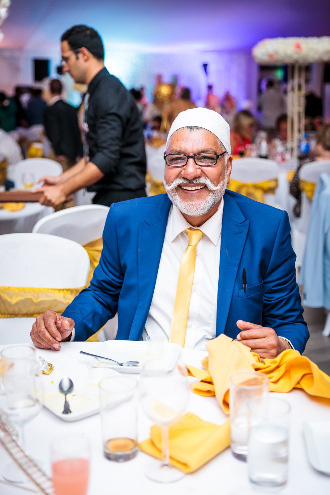 A smiling elder in a blue suit at a reception table dressed in yellow