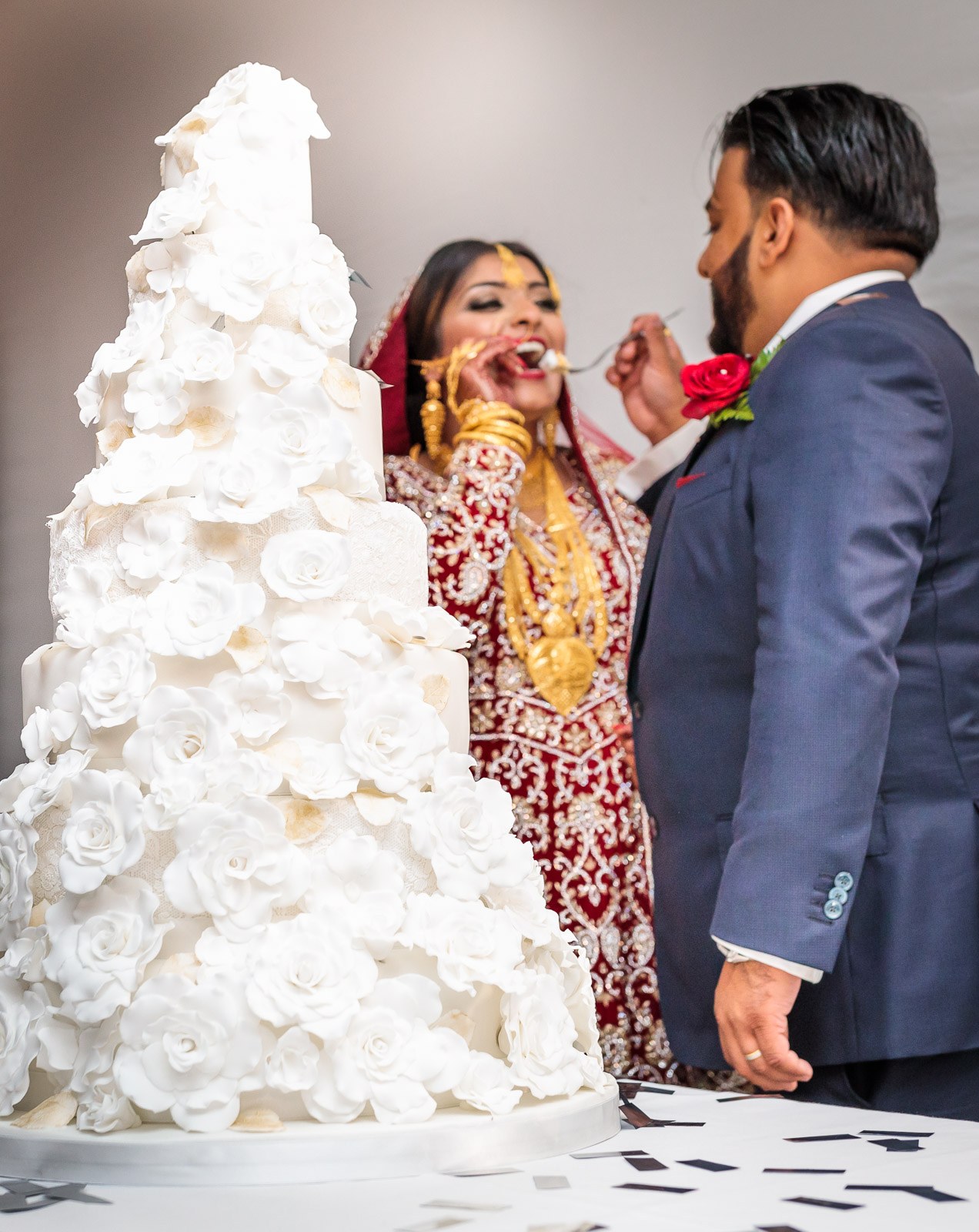 The groom feeds the bride cake beside the tall white flower cake