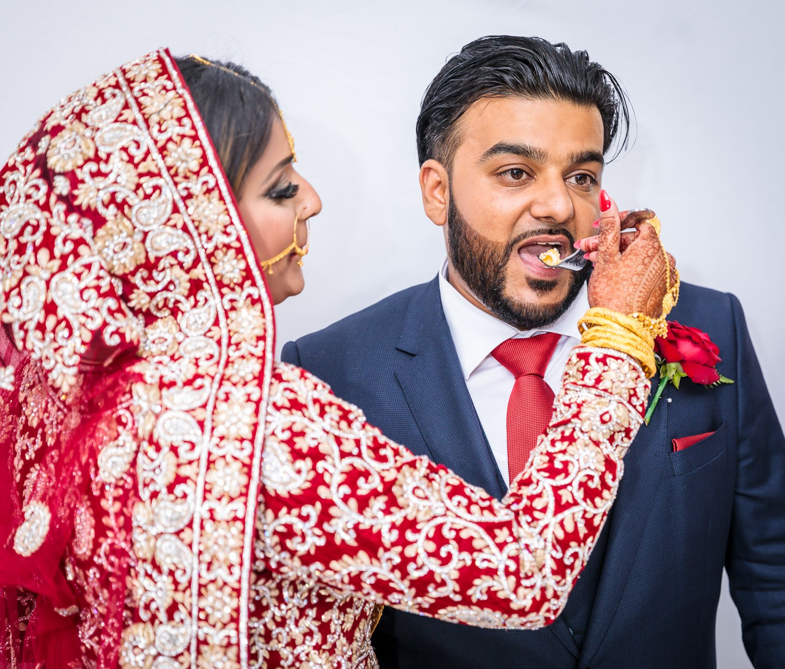 The bride feeds the groom a forkful of cake in her red bridal wear