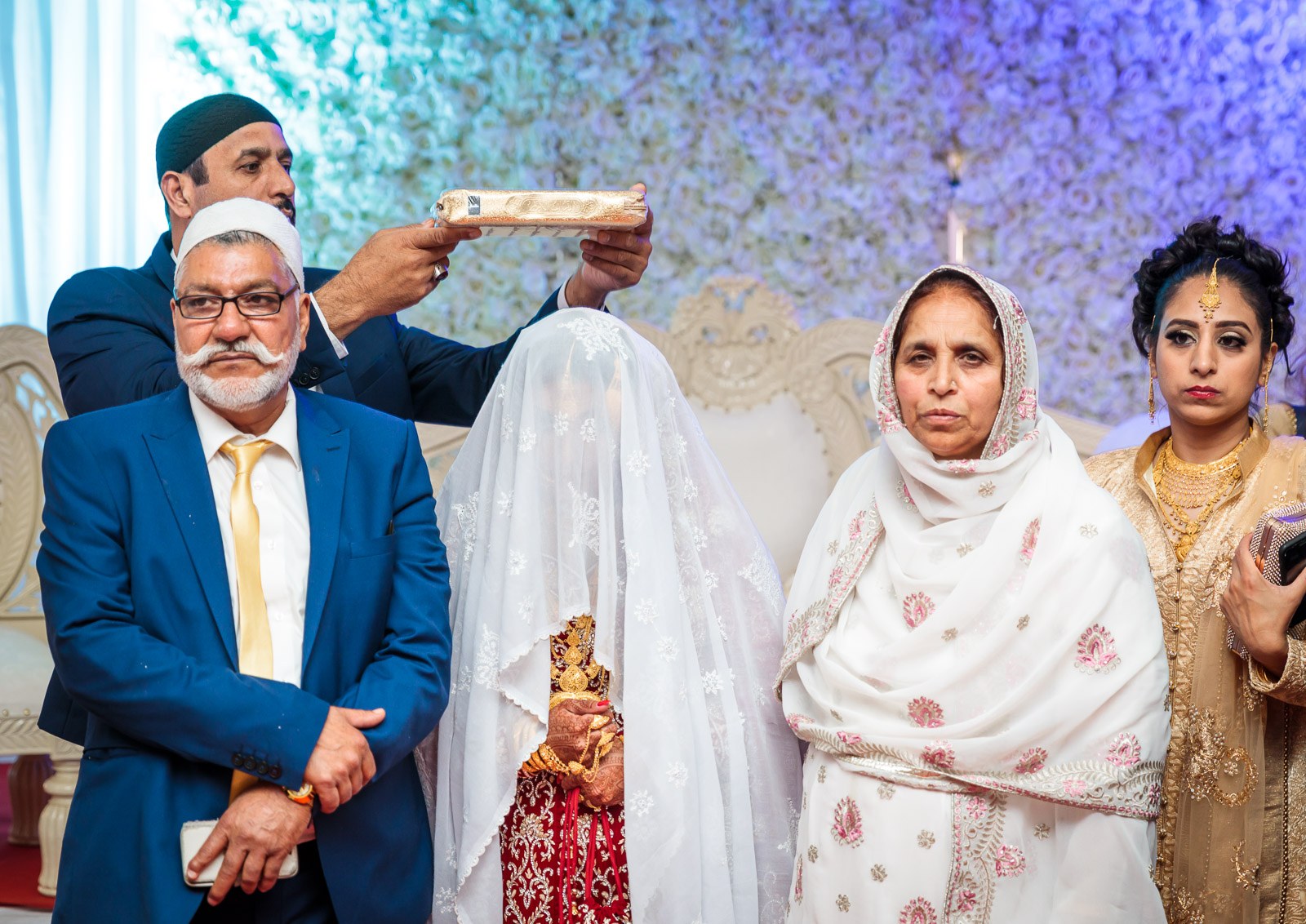 An elder holds the Quran over the veiled bride as her family stands close
