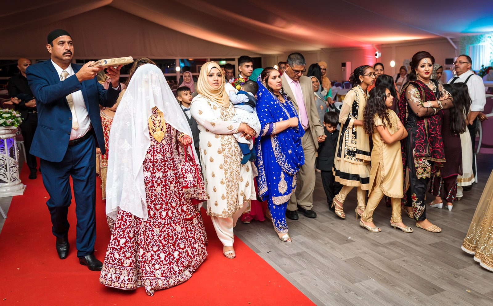 An elder holds the Quran over the departing bride along the red carpet