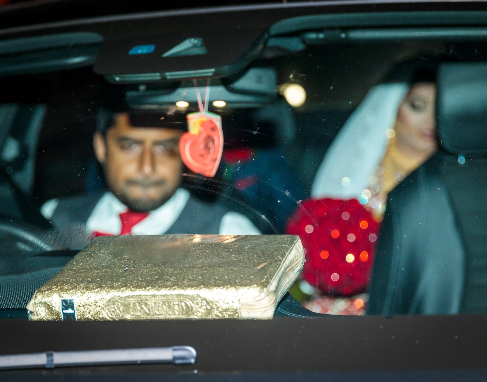 The veiled bride seen through the car windscreen at night, a gilded Quran on the dash