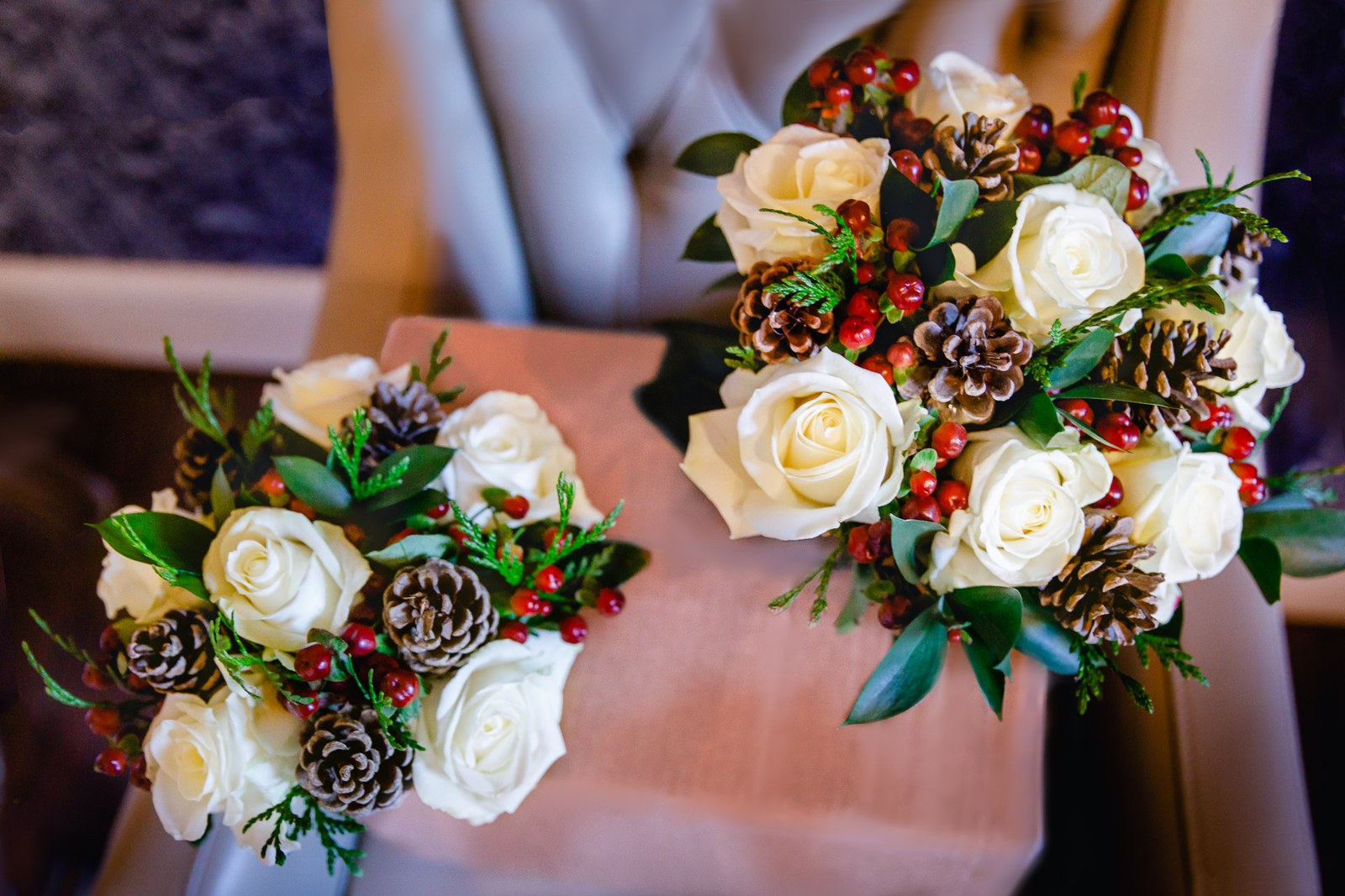 Two winter bouquets of white roses, pinecones and berries on a pink chair