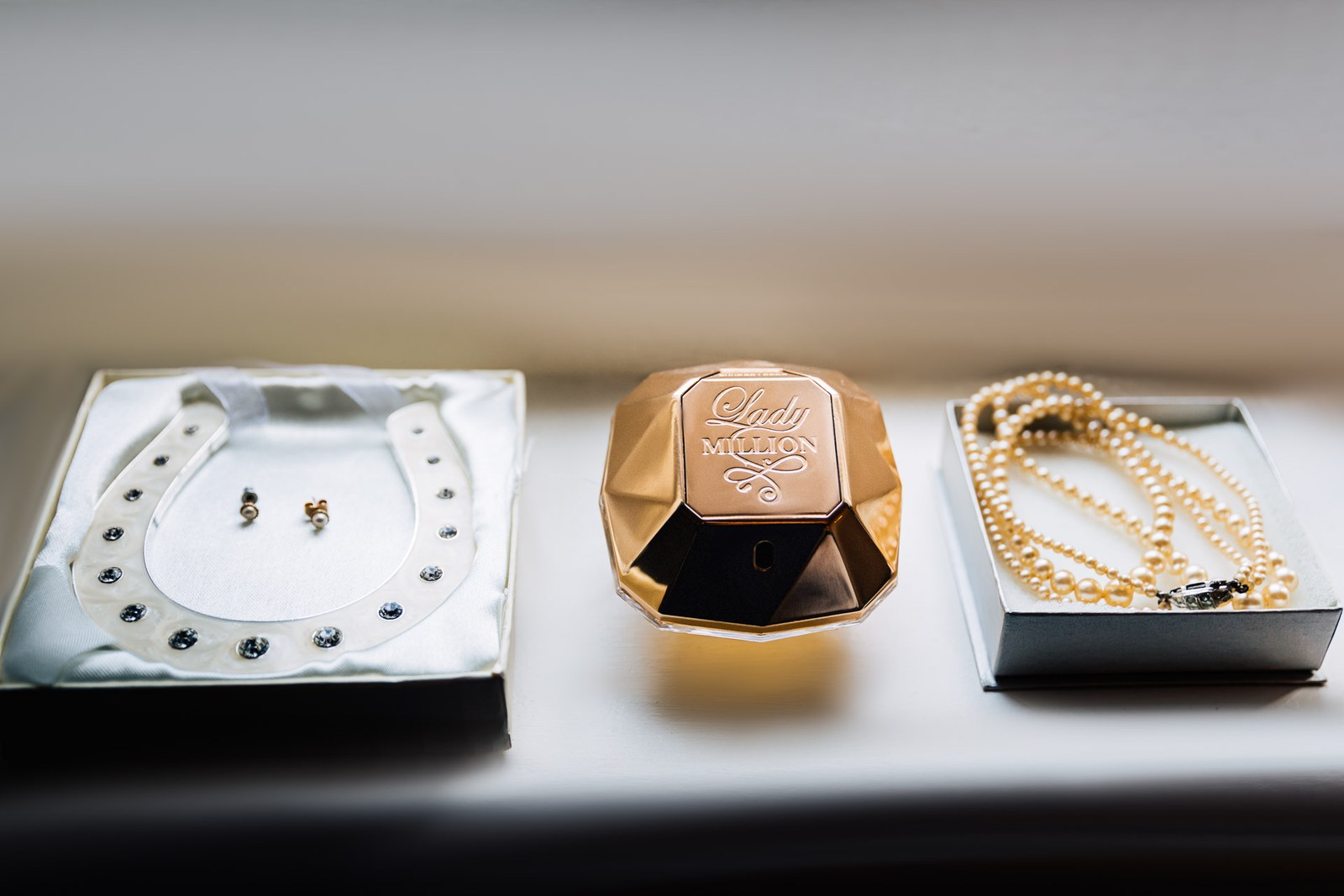 Flat lay of a jewelled horseshoe, perfume bottle and pearl necklace in their boxes