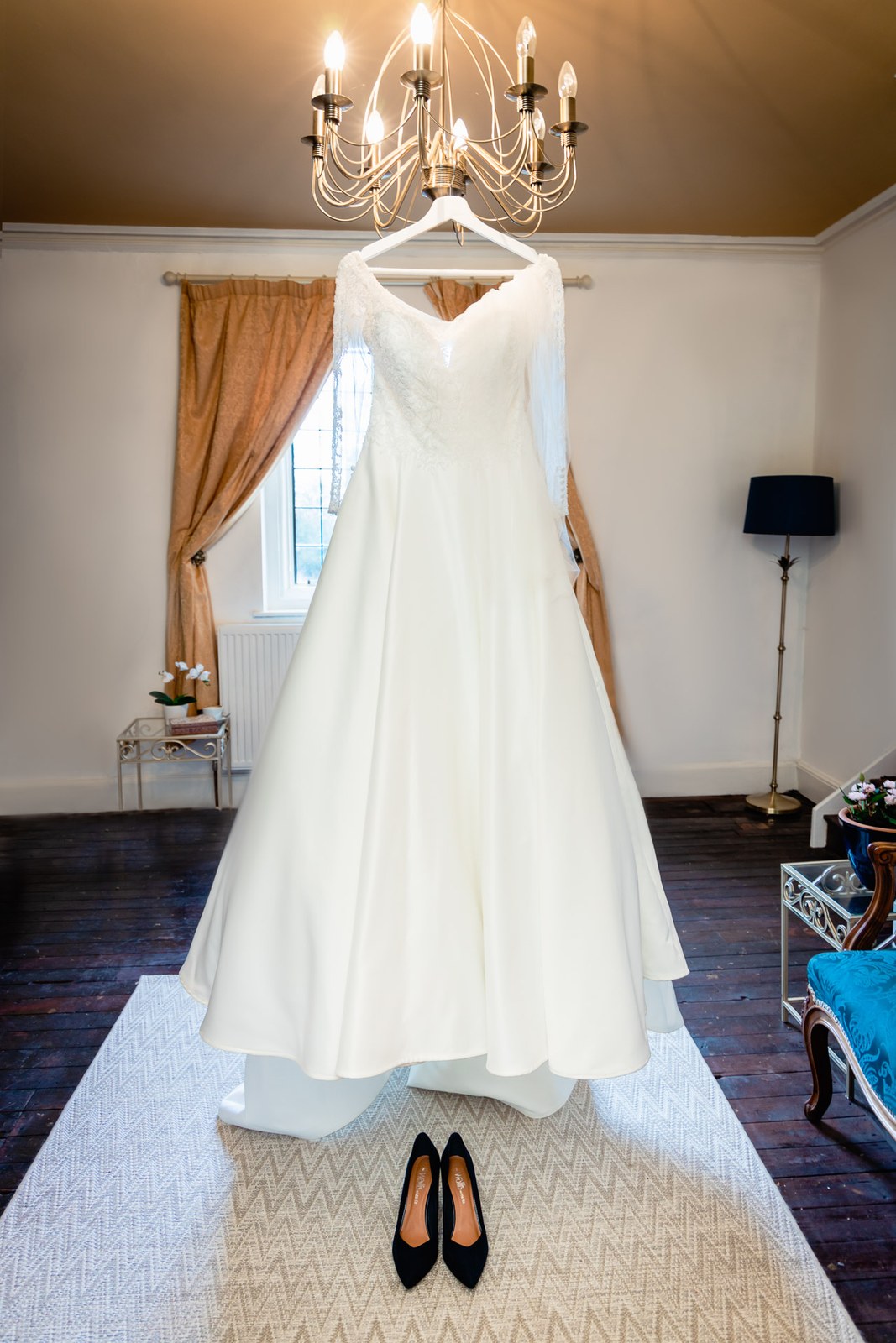 The bride's gown hangs from a chandelier above her black shoes
