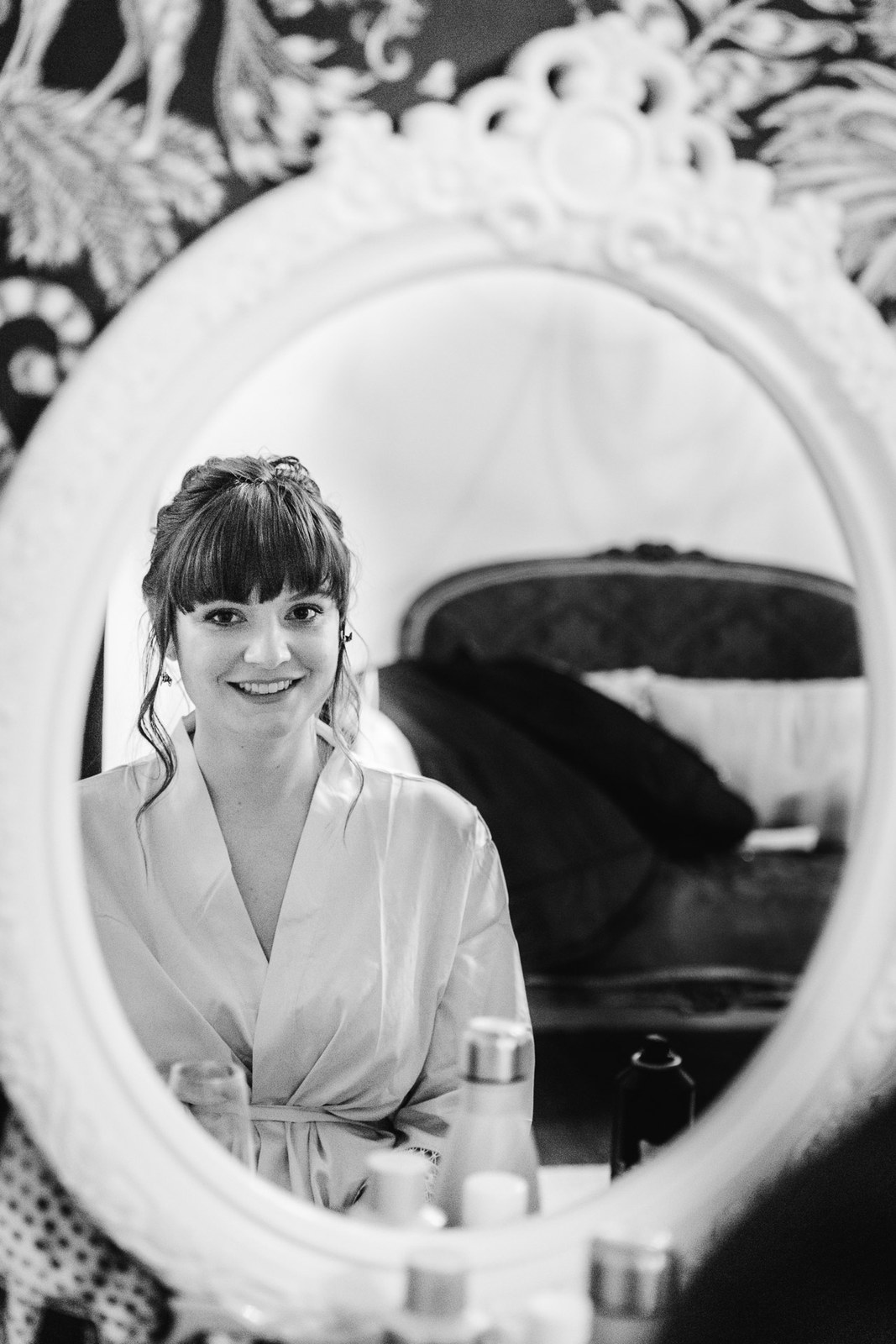 Black-and-white reflection of the bride smiling in an ornate oval mirror
