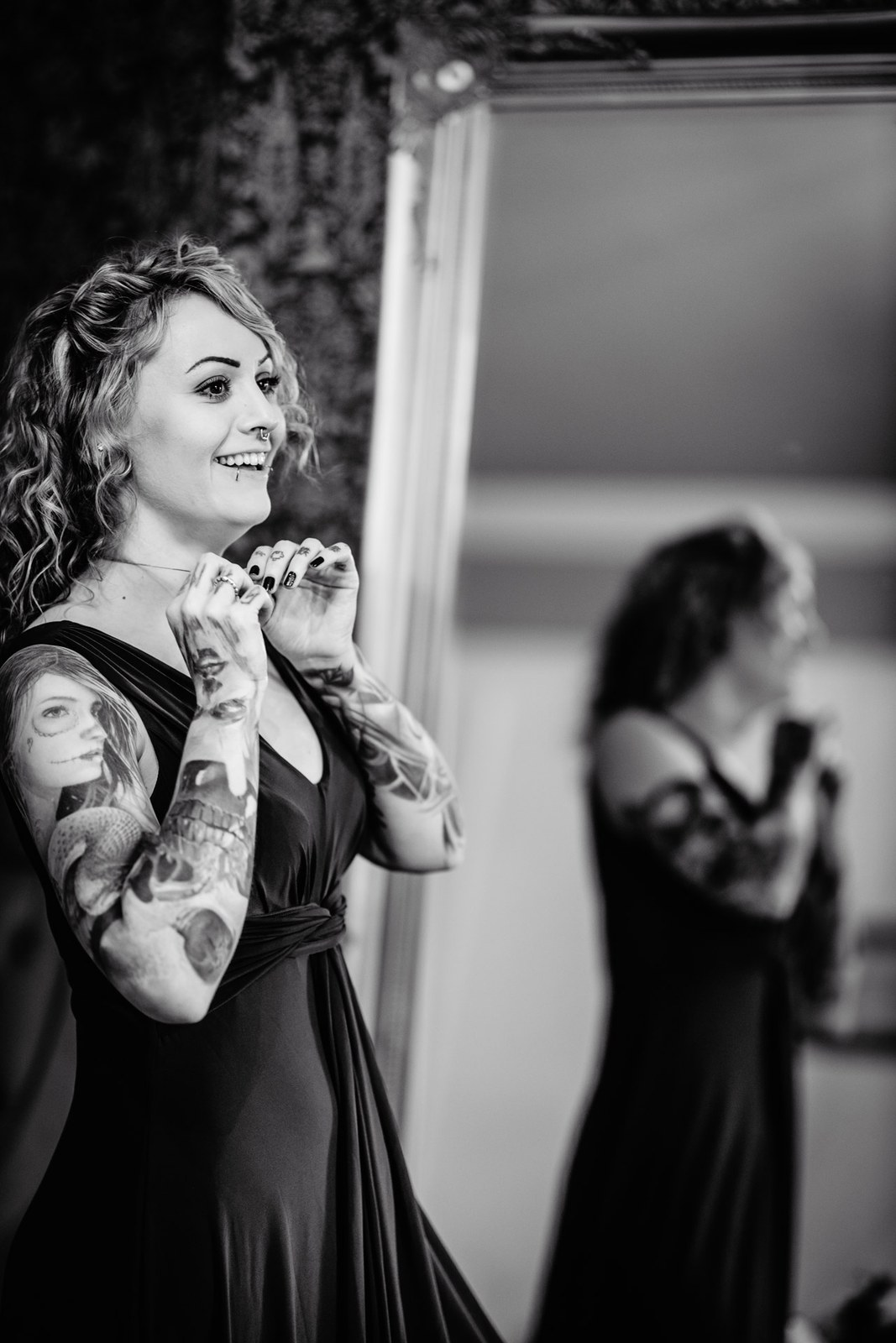 Black-and-white portrait of a smiling bridesmaid as another gets ready behind