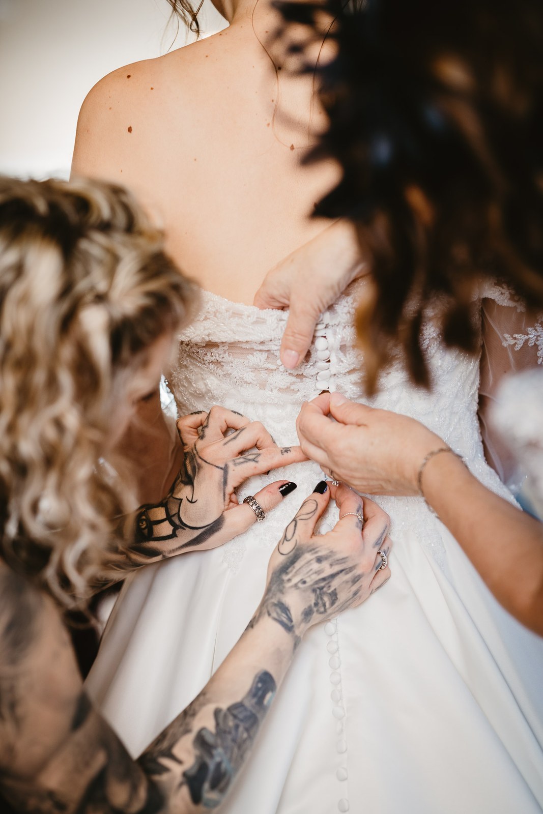 Helpers fasten the buttons at the back of the bride's gown