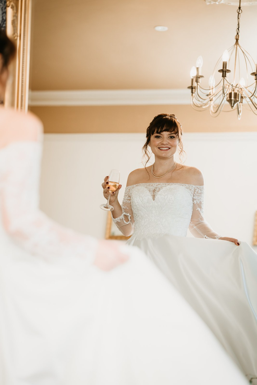 The bride laughs with a glass of champagne, a chandelier overhead
