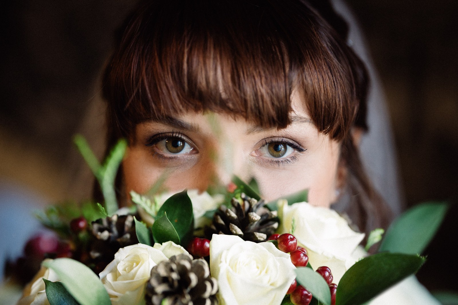 Close-up of the bride's eyes above her pinecone-and-rose bouquet