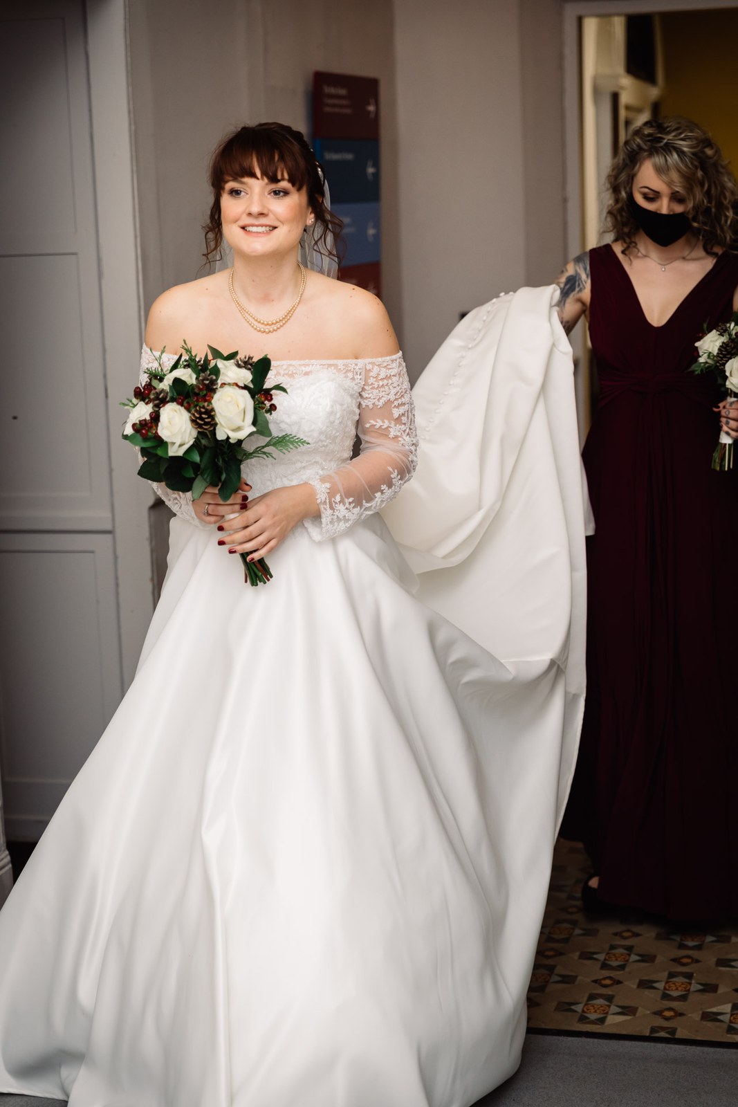 The bride waits in the doorway as a bridesmaid holds her train