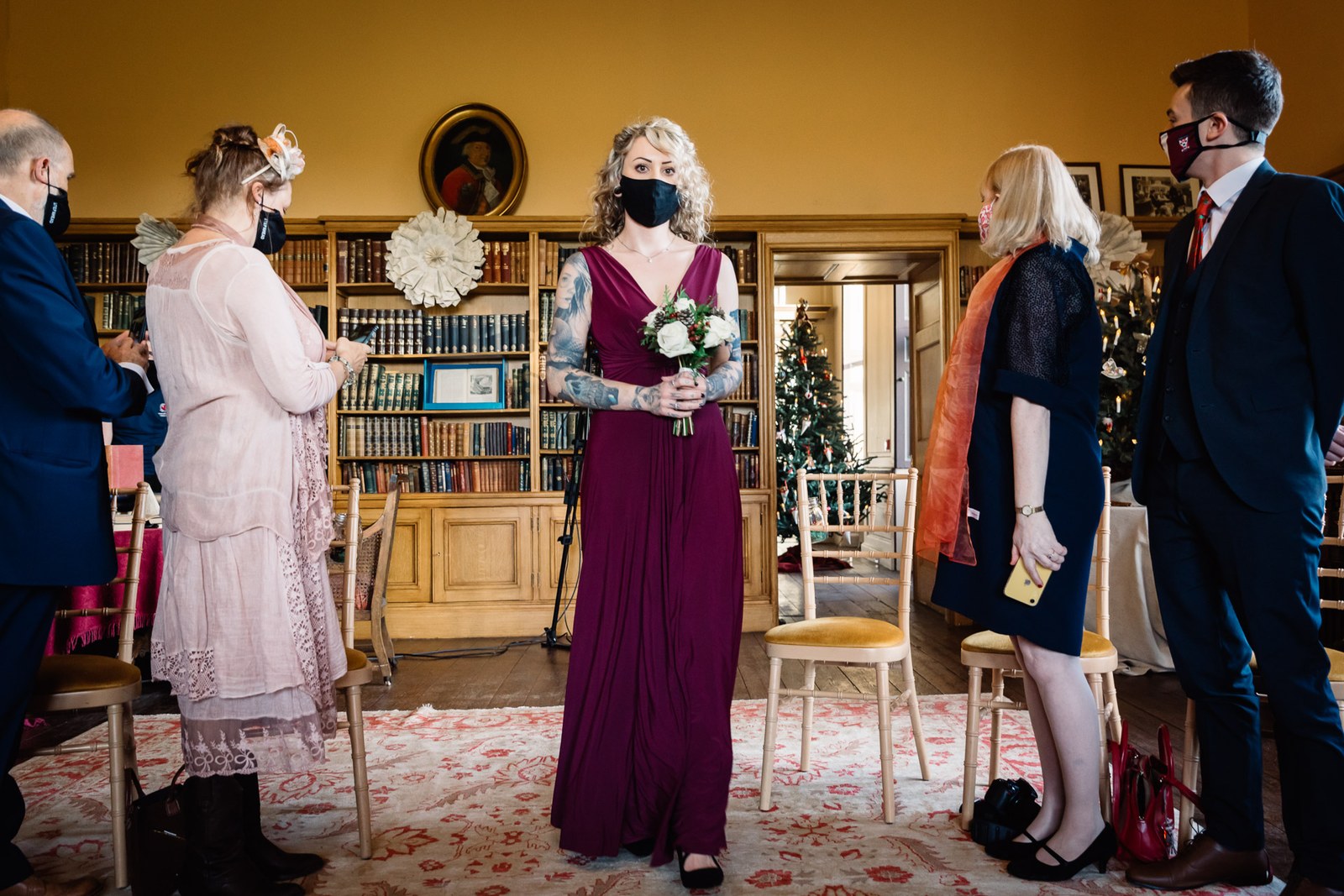 A bridesmaid in burgundy walks the aisle through the library