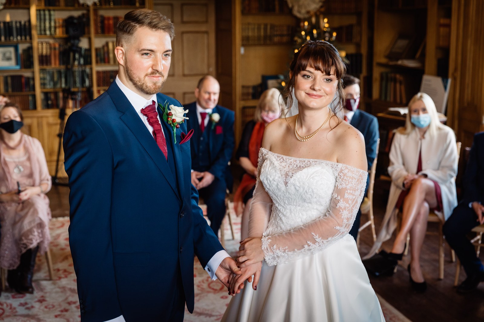 The couple stand together before their seated guests in the library