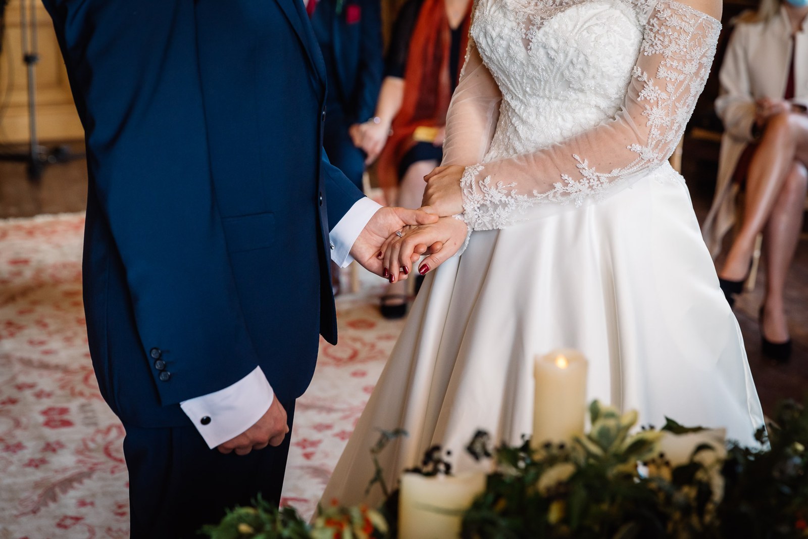 Close-up of the couple's clasped hands above a candle and winter greenery