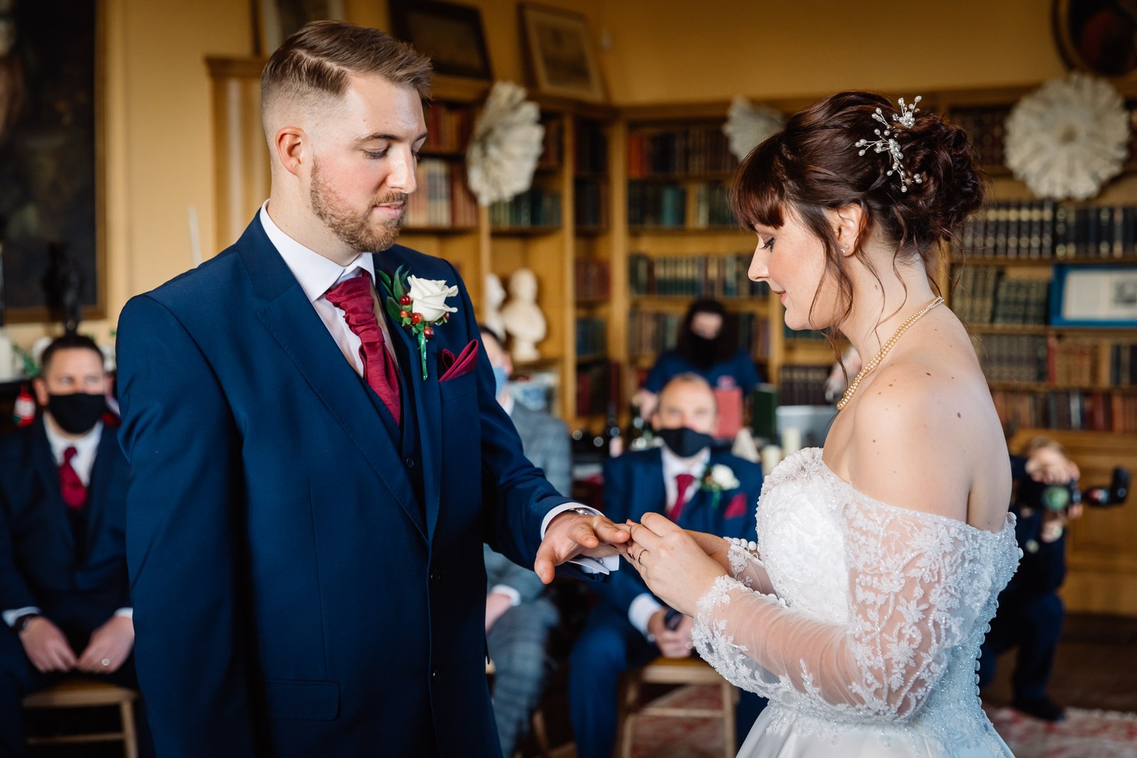 The bride places the ring on the groom's finger in the library