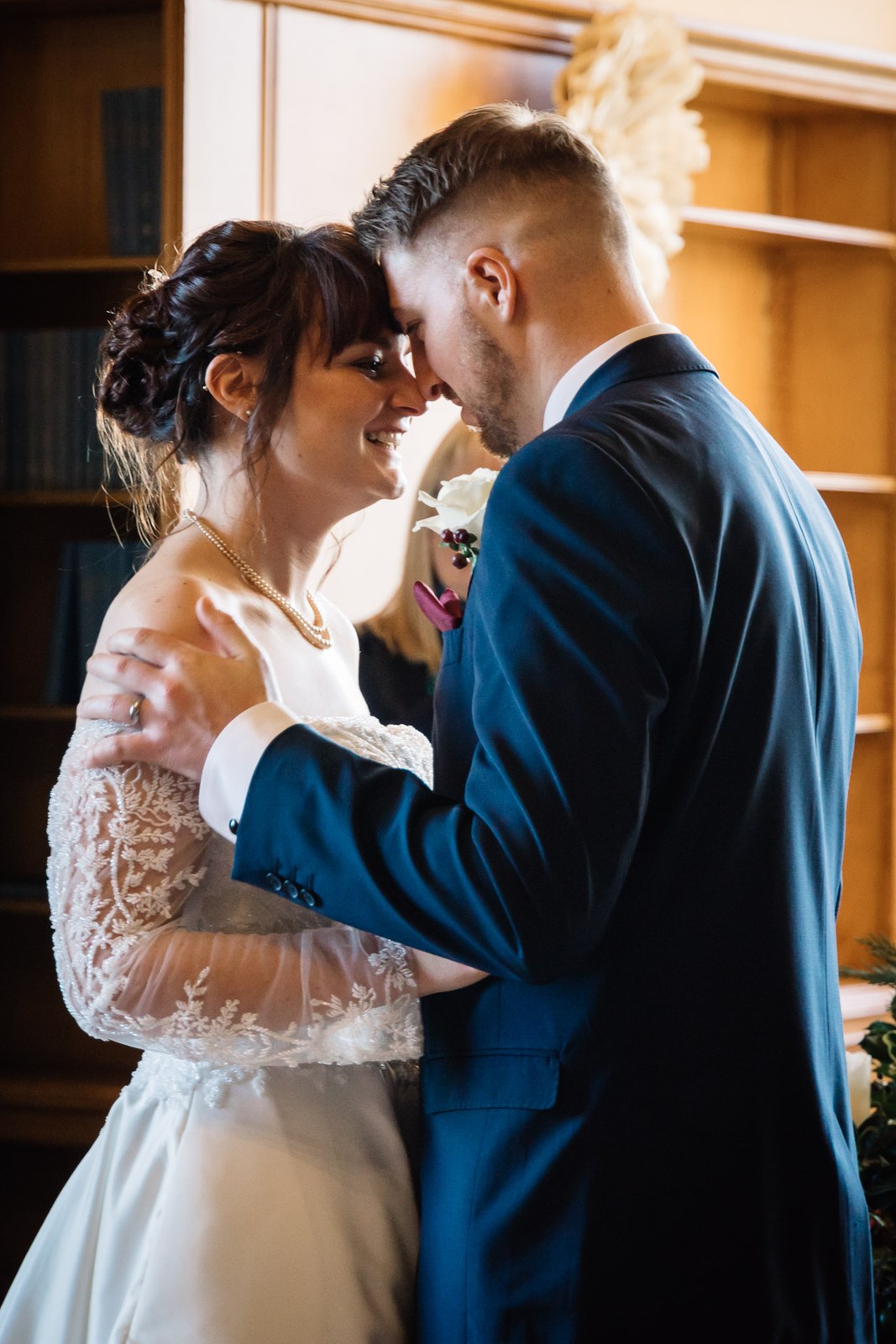 The couple stand forehead to forehead before the bookcases