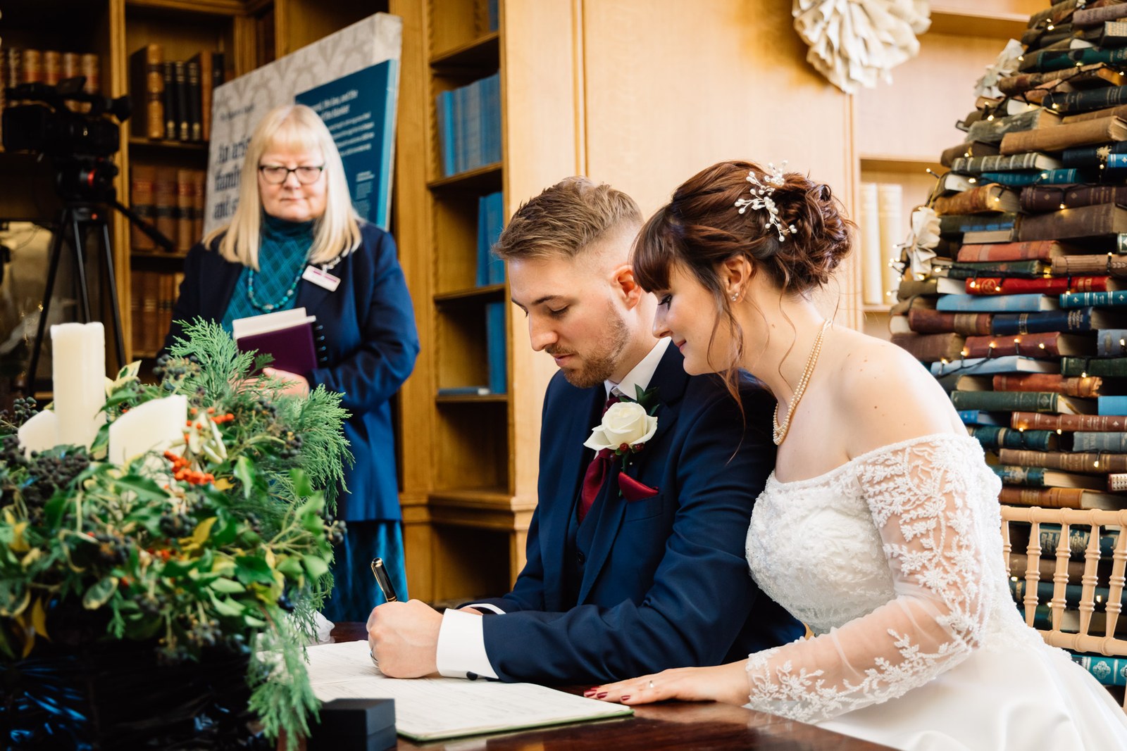 The couple sign the register at the desk as the celebrant looks on