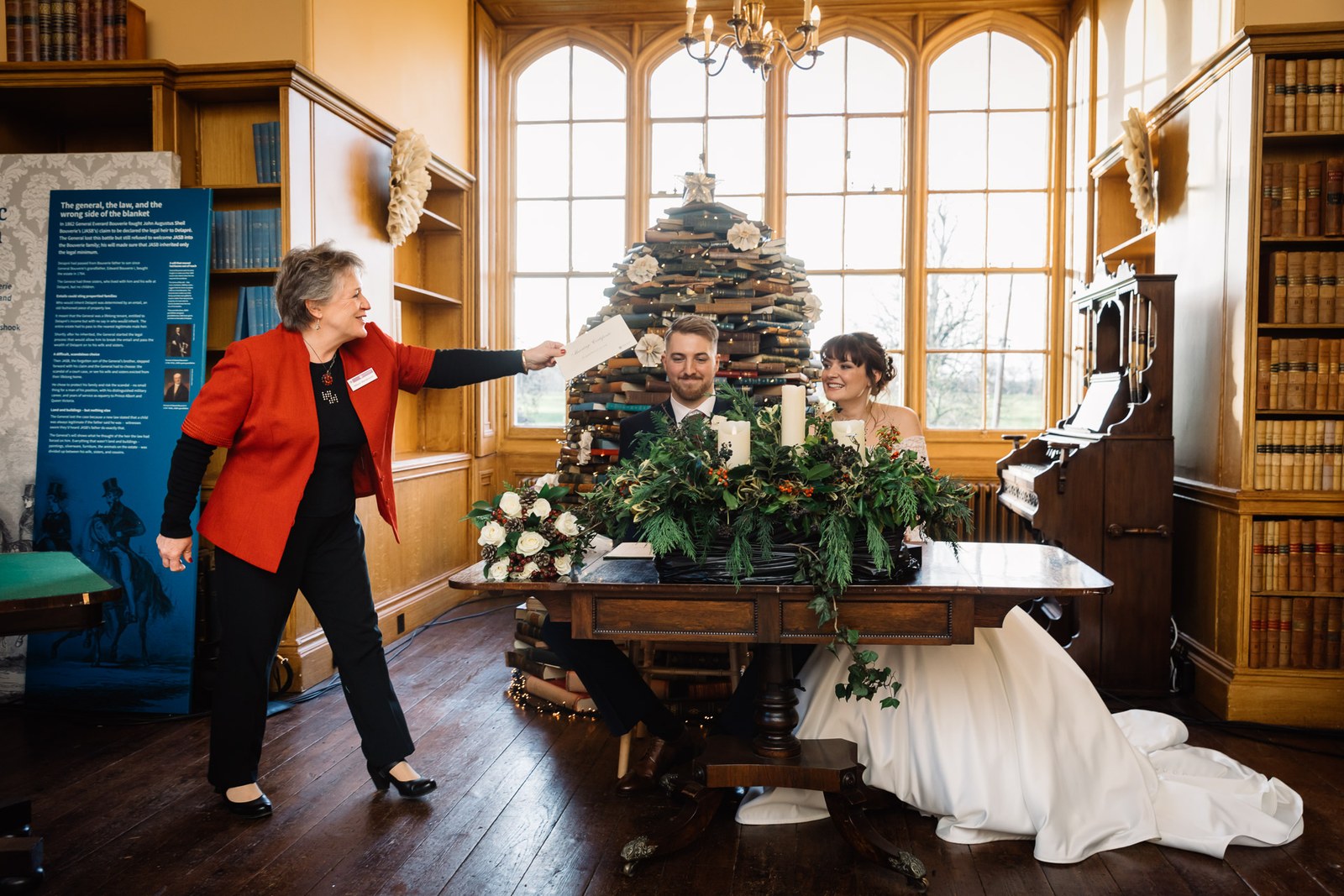 The registrar gestures as the couple sign beneath the arched library window