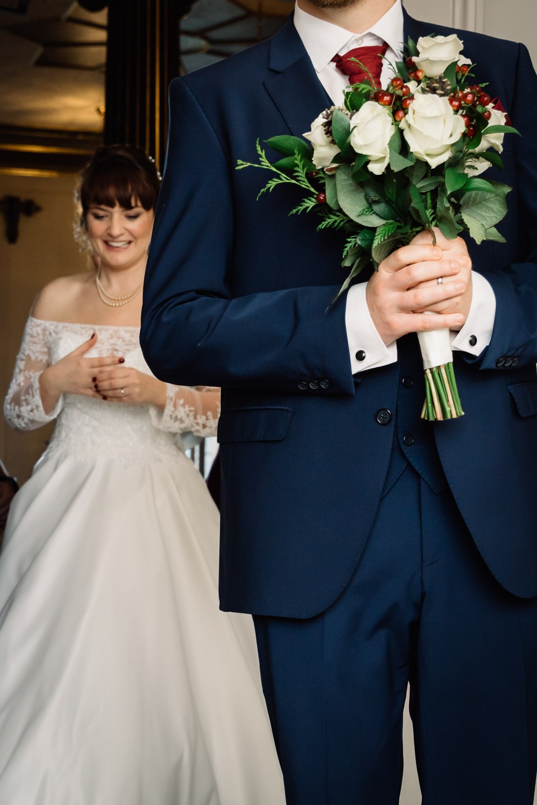 The bride tucks under the groom's arm as he holds her winter bouquet