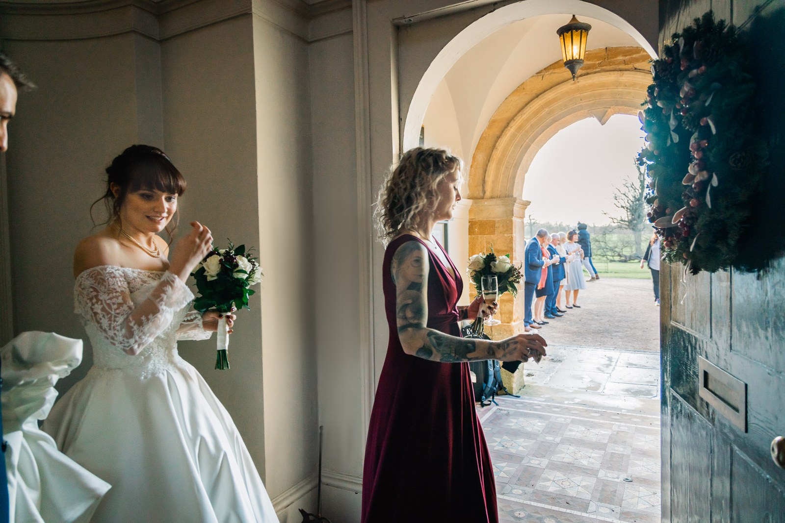 The bride waits by the wreath-hung door of Delapre Abbey as guests gather outside