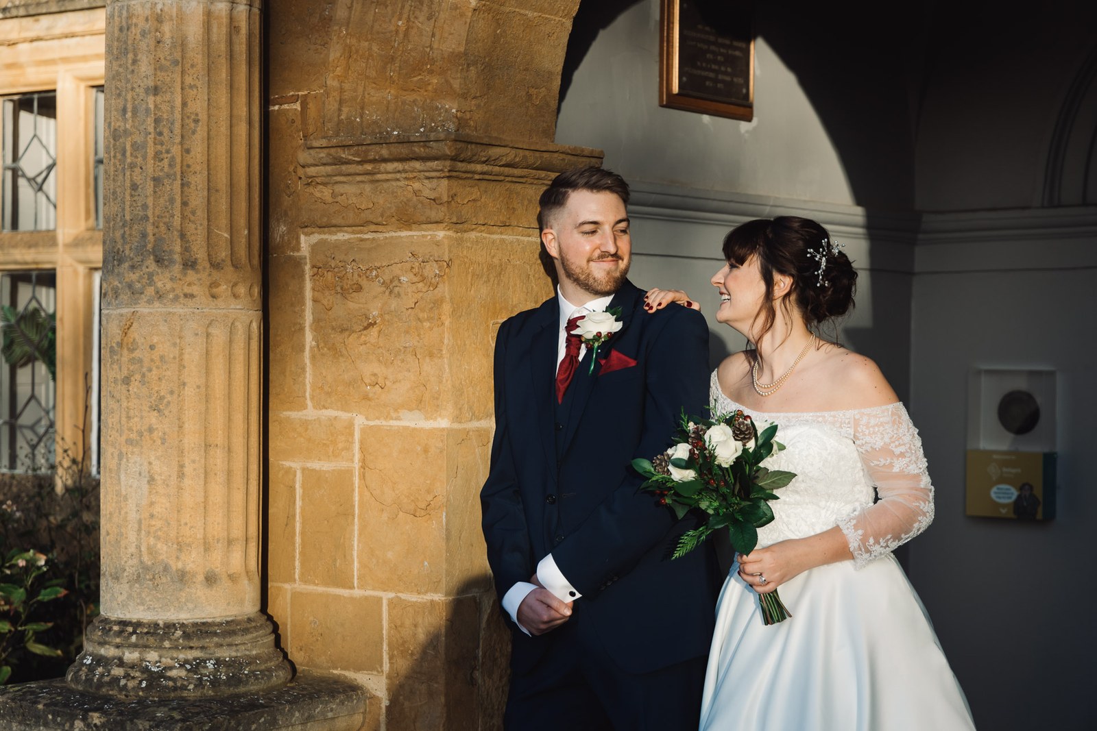 The couple pause by a stone column beneath the arched porch of Delapre Abbey