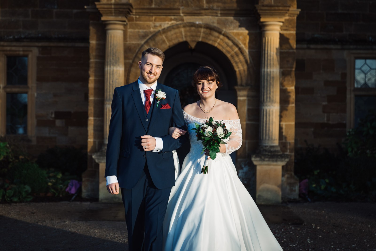 The newlyweds step out from the arched entrance of Delapre Abbey in golden light