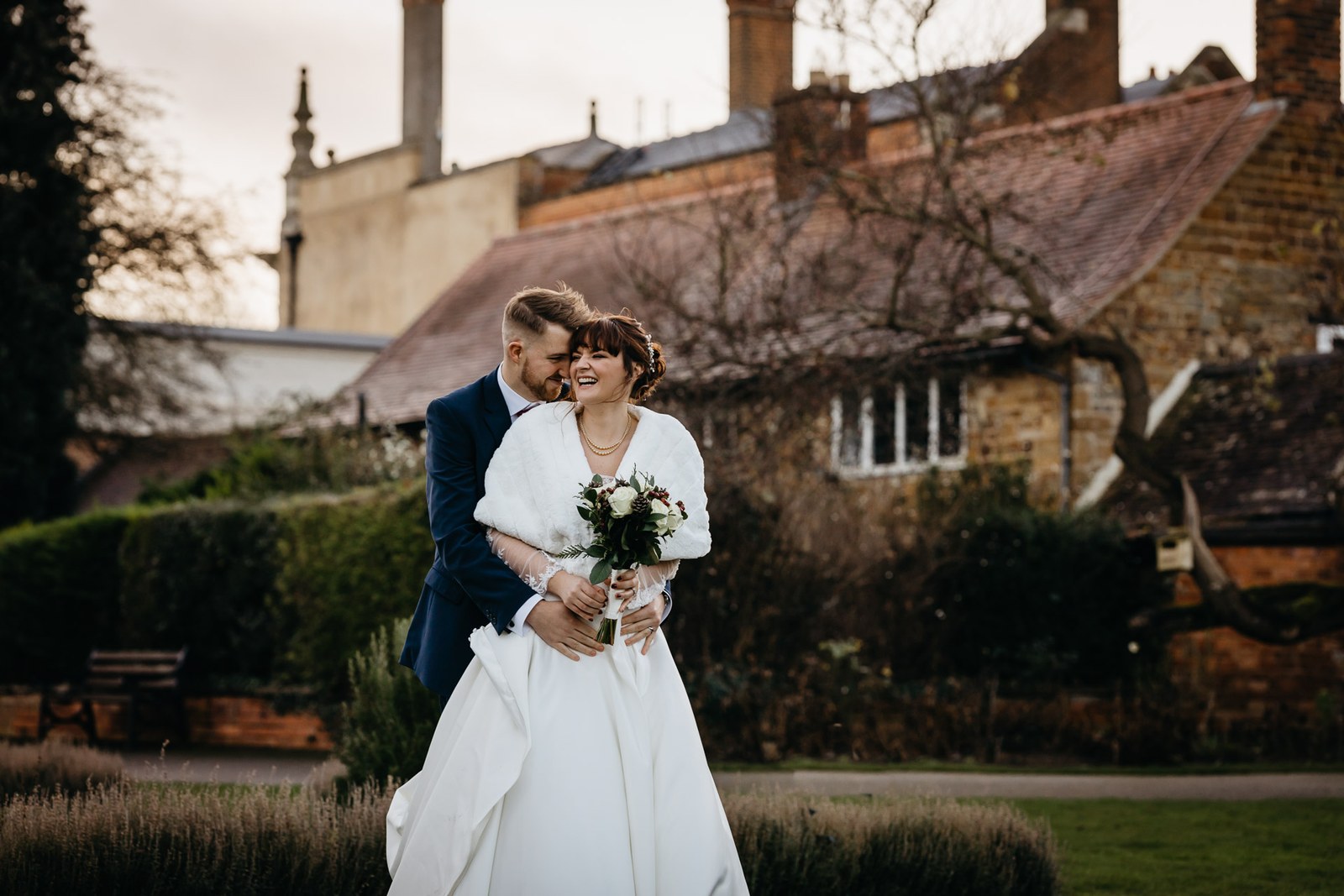 The couple hold each other beside the honey-stone walls of Delapre Abbey