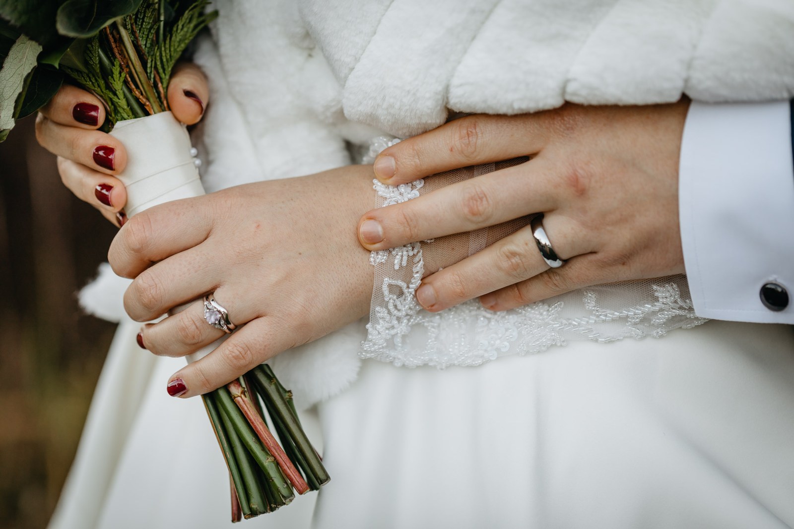 Close-up of the couple's hands over the bouquet, showing their wedding rings