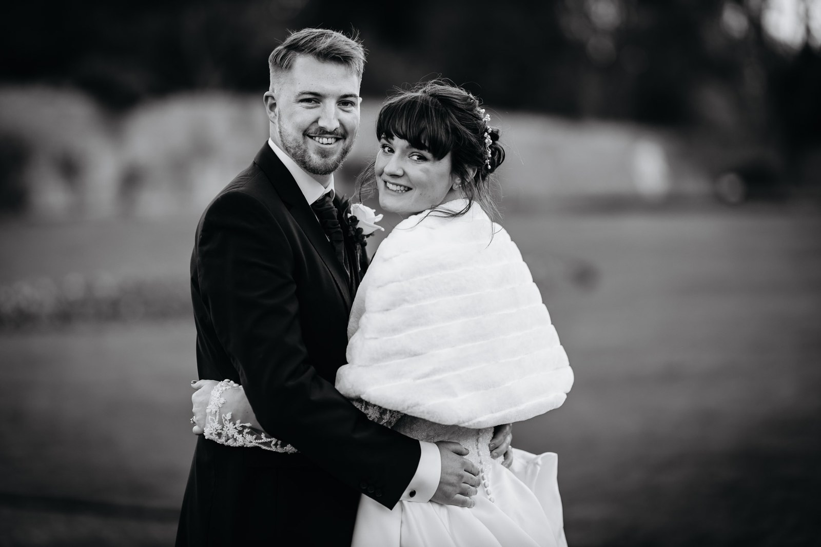 Black-and-white portrait of the couple embracing, the bride in a fur stole