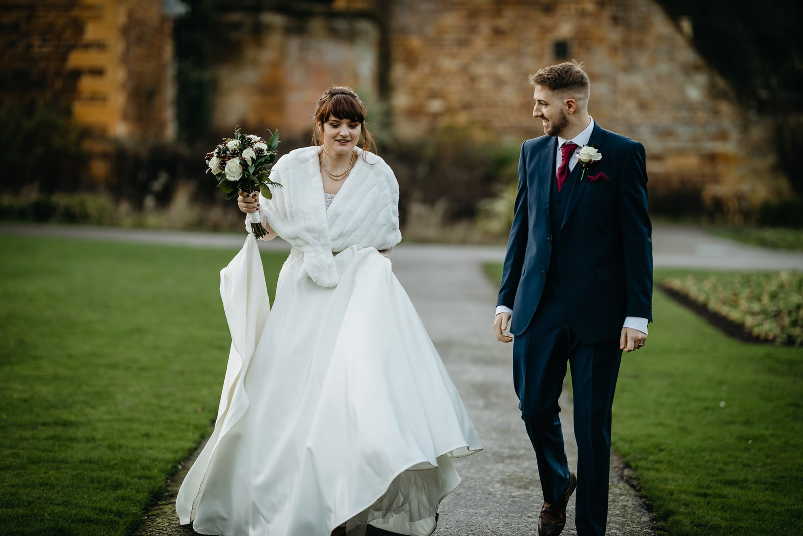 The couple walk a path beside the old stone wall of Delapre Abbey