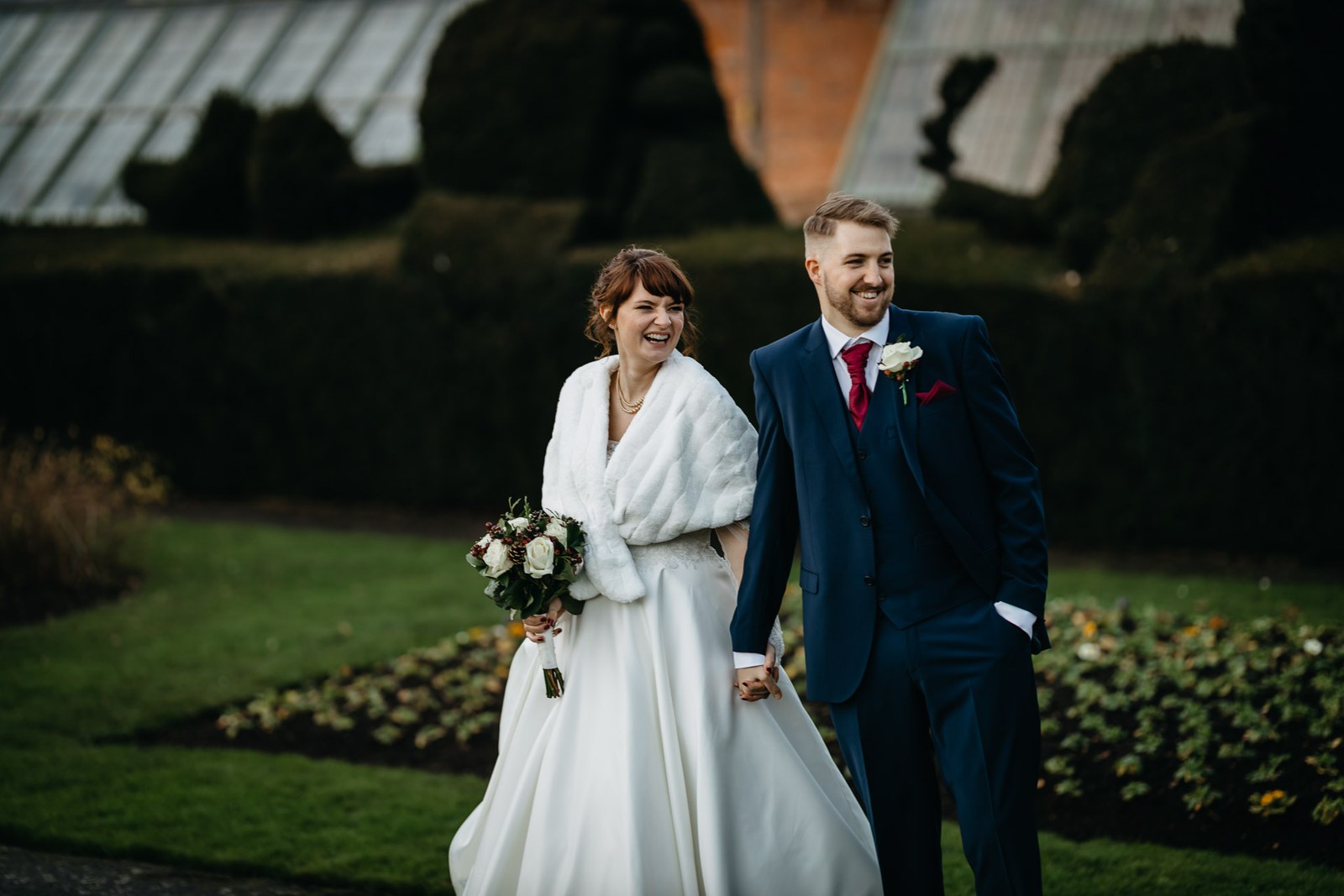 Bride and groom walk the lawn past the topiary hedges of Delapre Abbey