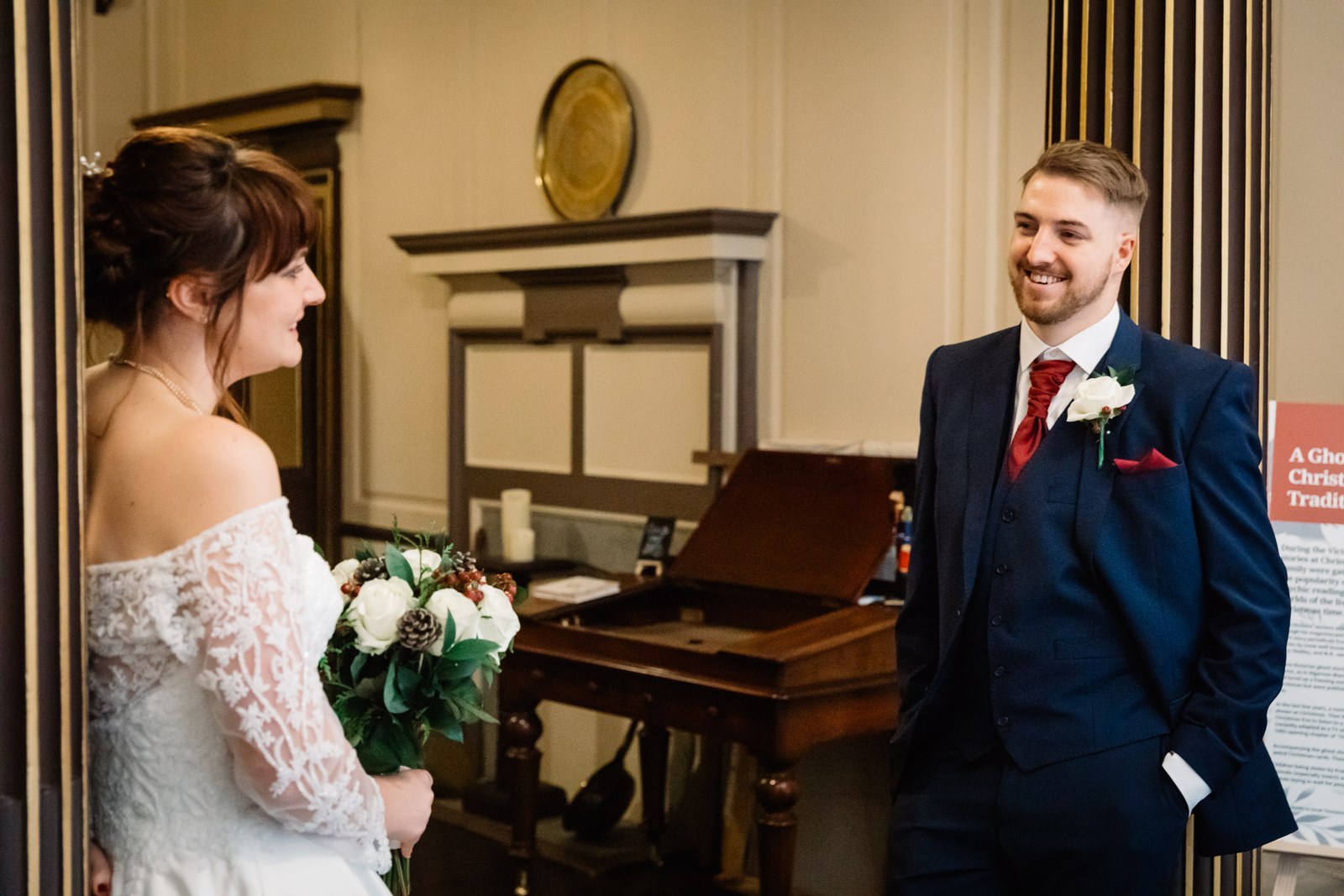 The couple stand by the fireplace and piano, the groom smiling