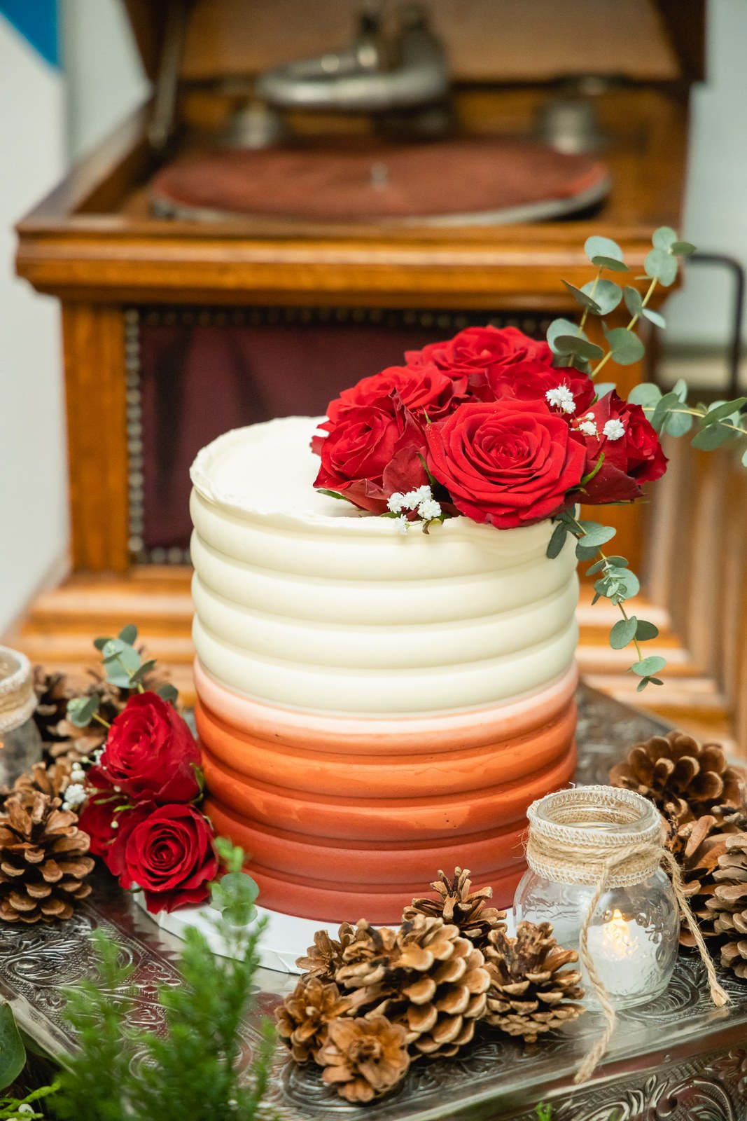 The ombre winter cake trimmed with red roses and pinecones on a gramophone cabinet