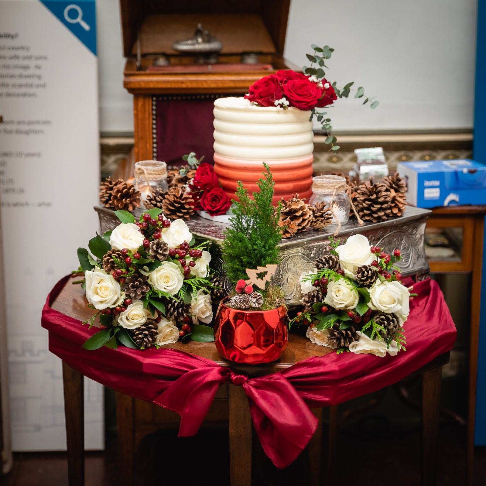 The wedding cake on a draped table with pinecones, roses and a red glass vase
