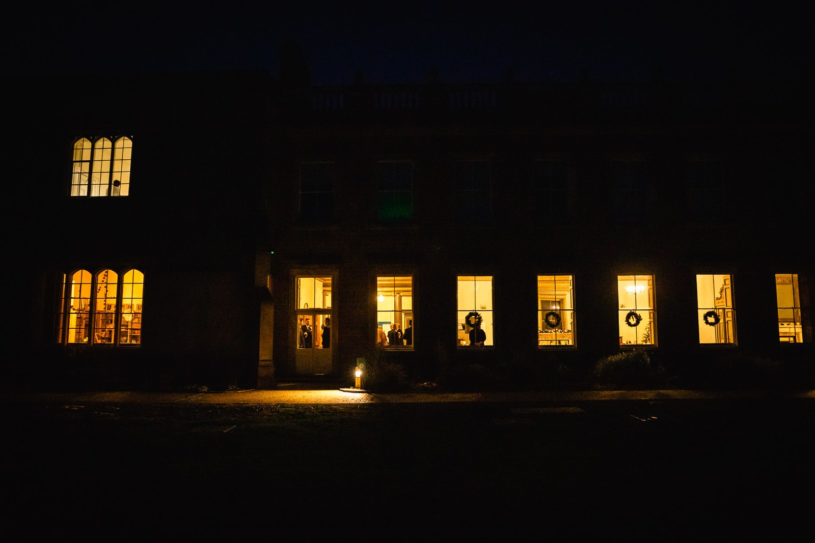 Delapre Abbey at night, its arched windows glowing warmly
