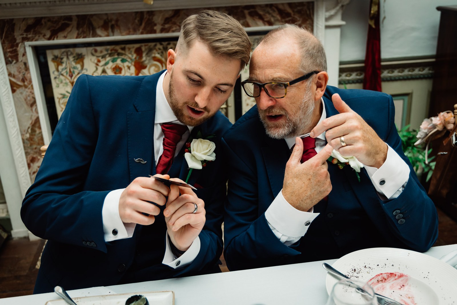 The groom and an older man examine a ring at the table