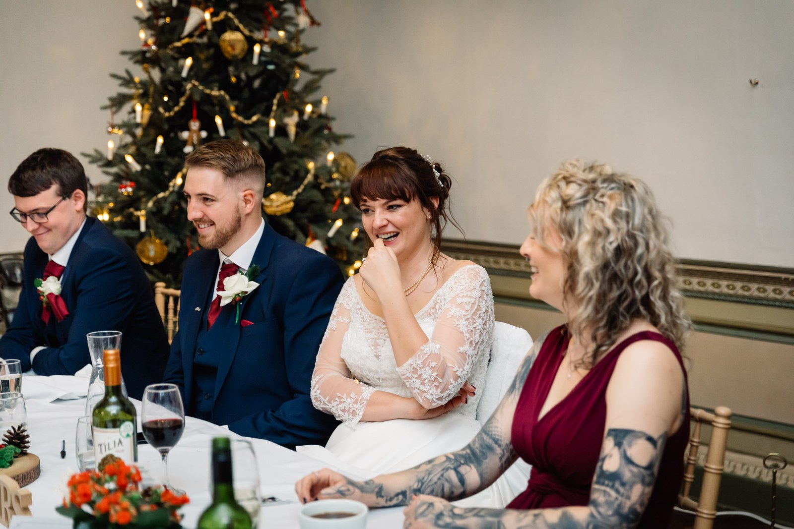 The couple laugh at the top table beside a decorated Christmas tree